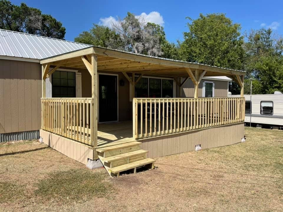Tan mobile home with a small covered wooden porch and steps in a sunny yard