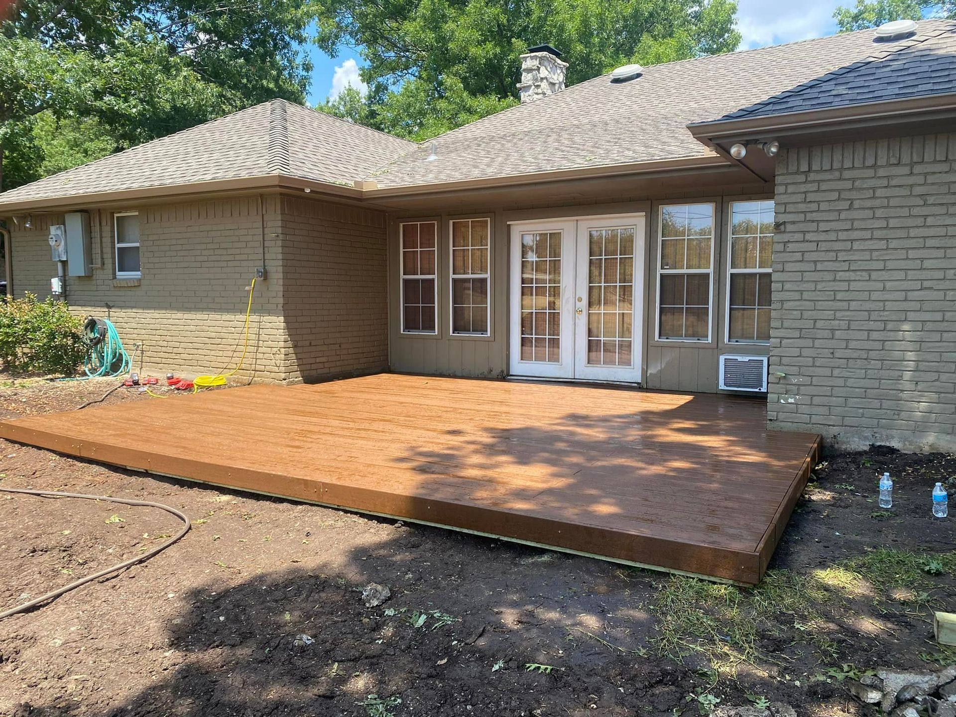 Brick house patio with a new wooden deck in the backyard under trees