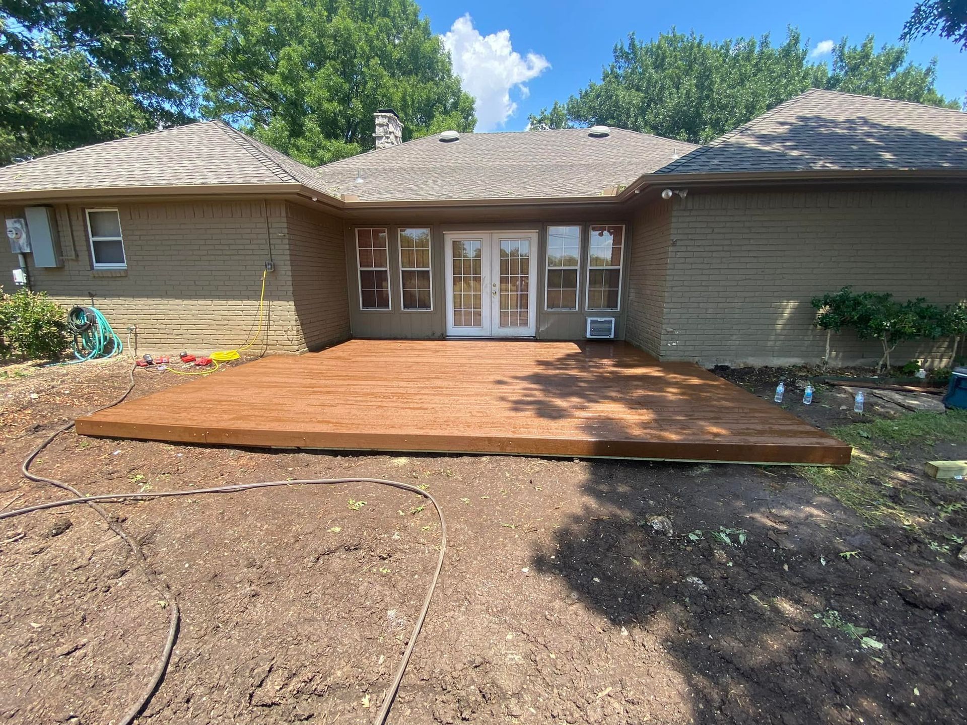 Backyard house patio with a newly stained wooden deck and french doors under a sunny sky
