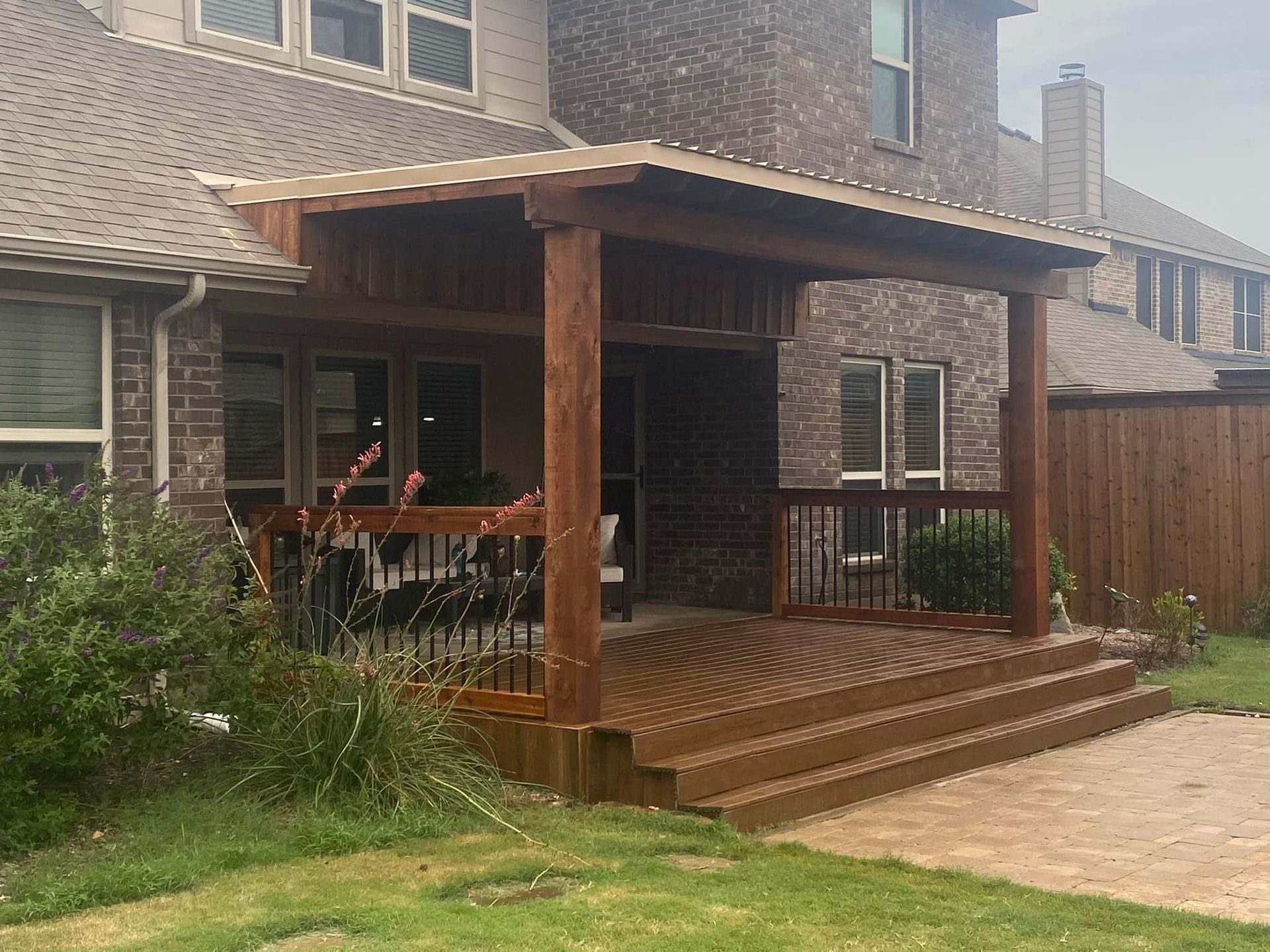 Brick house with a wooden porch, steps, and railing beside a paved driveway.