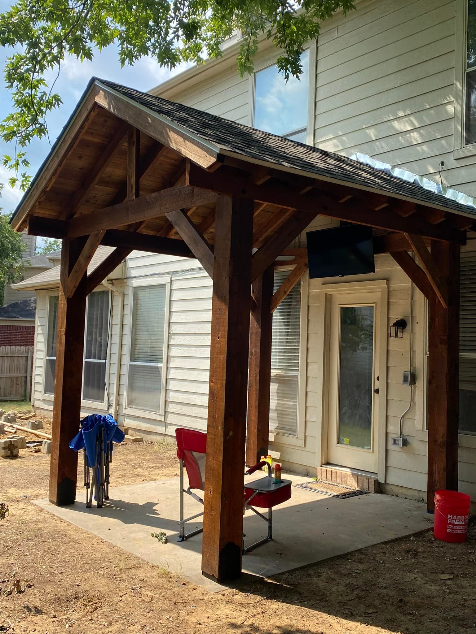 Wooden pergola patio beside a house with chairs, tools, and a concrete slab under construction