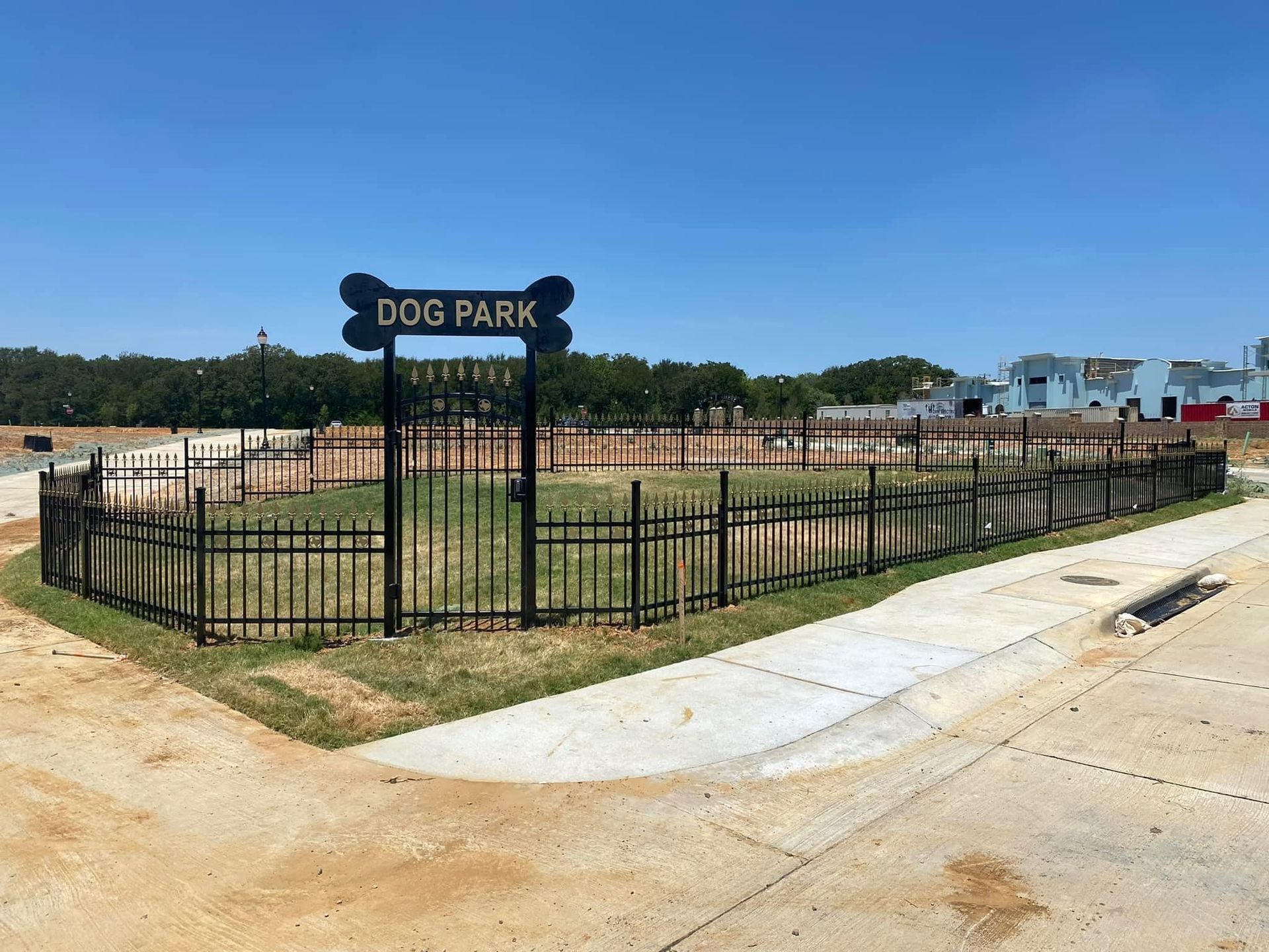 Fenced dog park with “DOG PARK” sign beside a sidewalk under a clear blue sky
