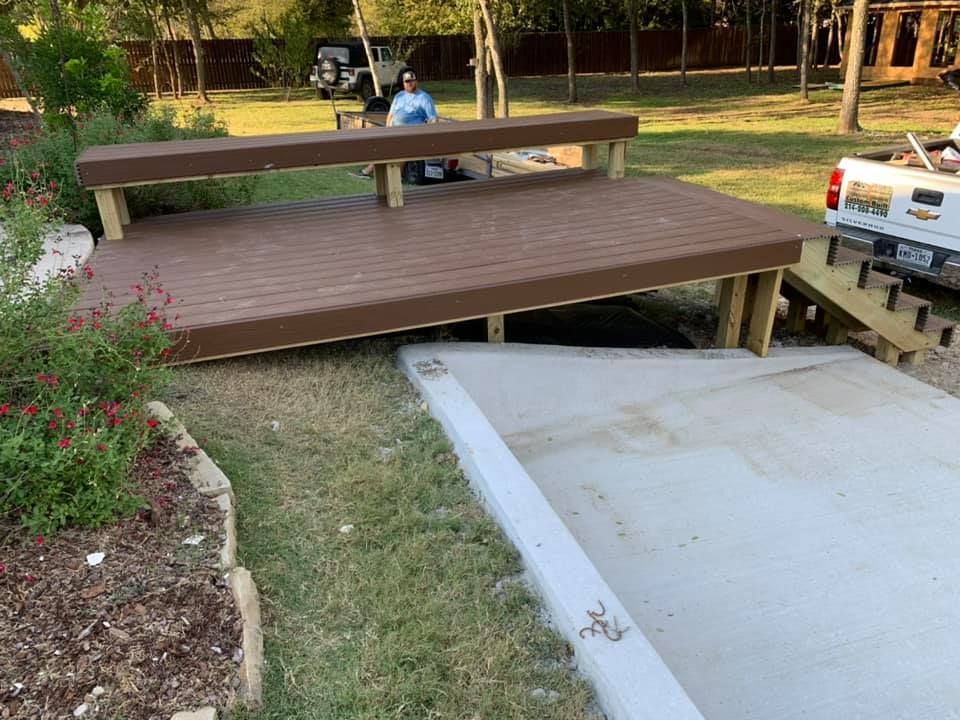 Wooden bench platform over a concrete ramp in a park, with flowers and a parked truck nearby.