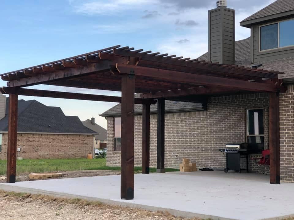 Backyard patio with a wooden pergola attached to a brick house and a concrete slab underneath.