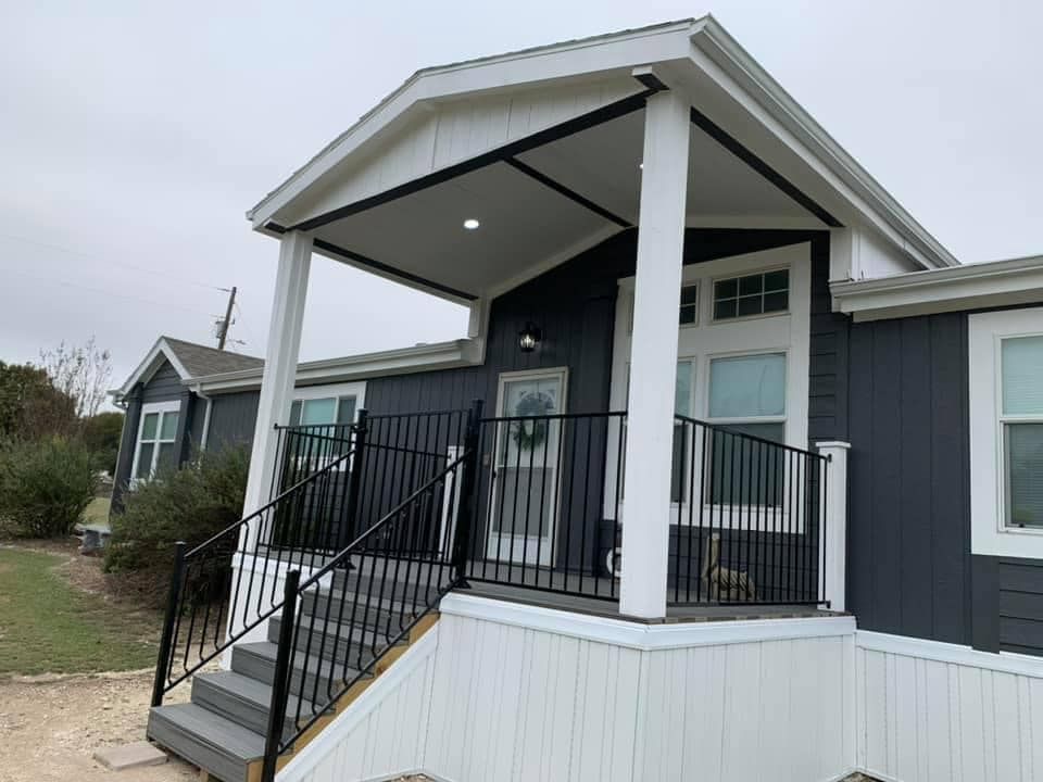 Front porch entrance with black railings, gray siding, and white trim on a small house