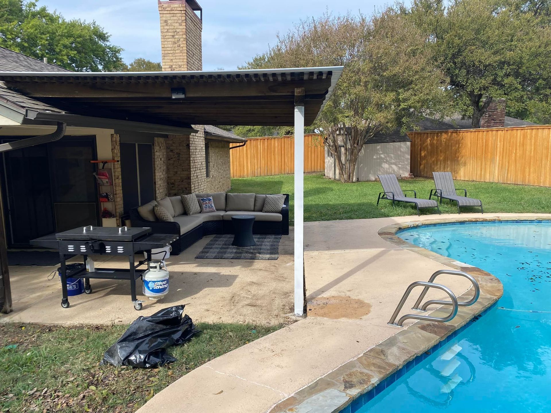 Backyard patio with covered seating area beside a swimming pool and fenced lawn
