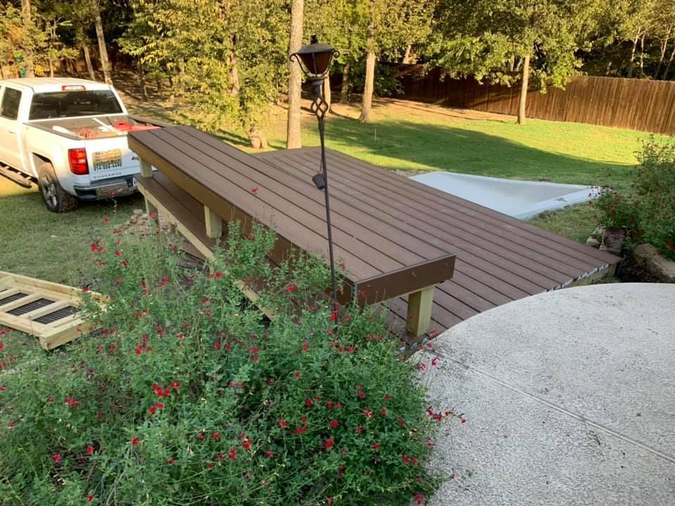 White pickup beside a wooden bridge over a landscaped garden path with red flowers