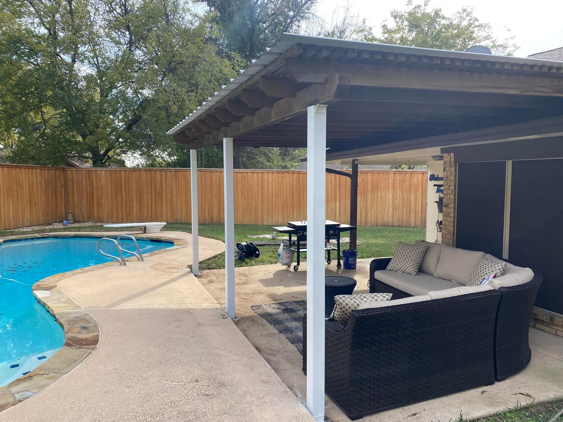 Backyard pool with covered patio seating, wooden fence, and tan concrete deck