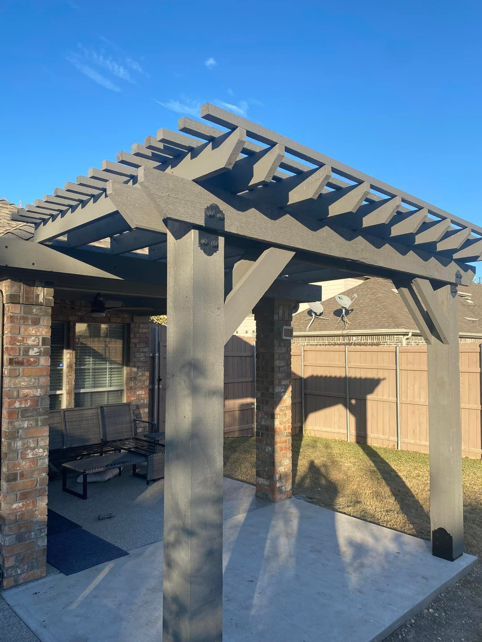 Backyard patio pergola with concrete posts and a slatted roof under a blue sky