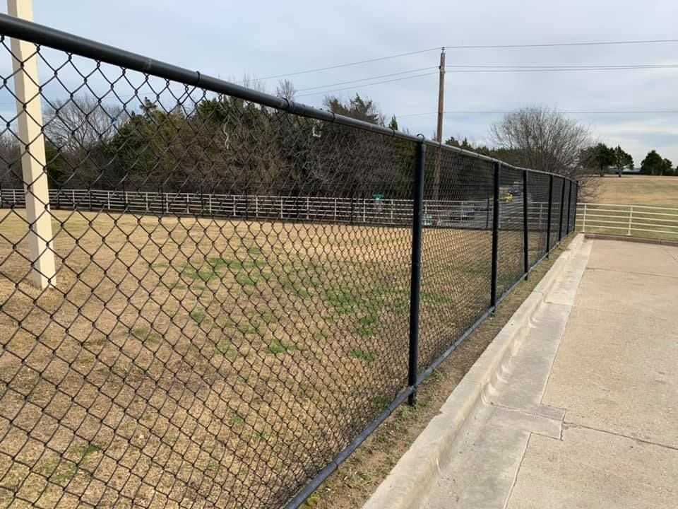 Chain-link fence along a dry grassy field beside a concrete sidewalk