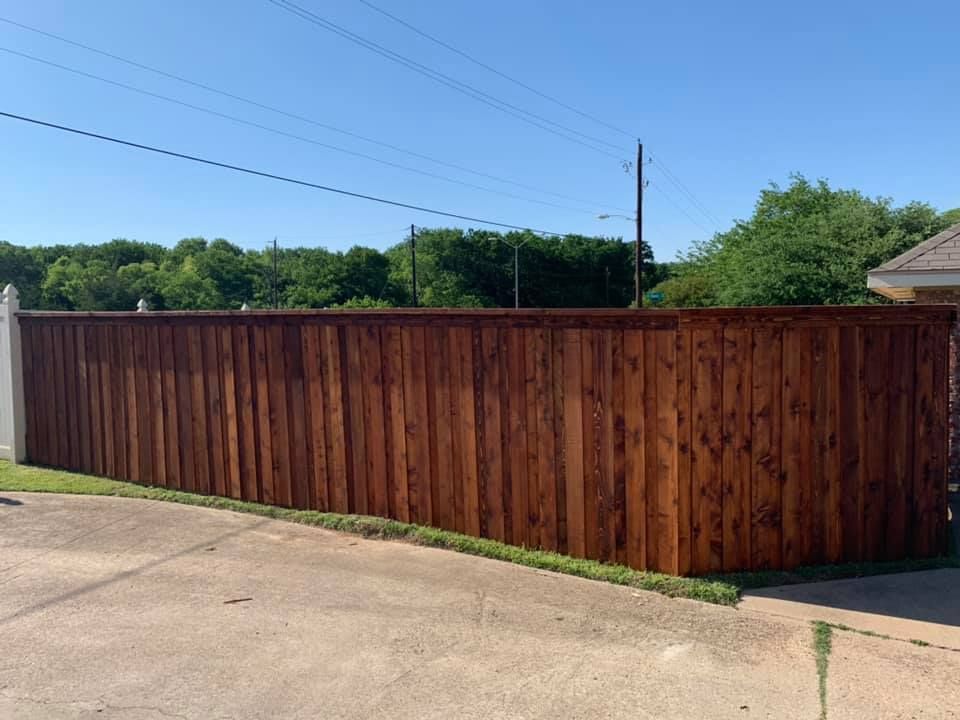 Wooden privacy fence beside a concrete driveway under a clear blue sky