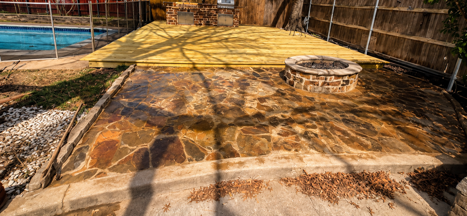 Stone patio path in a fenced backyard, with a circular fire pit and yellow paving in the background