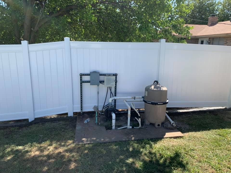 Outdoor pool equipment setup beside a white vinyl fence in a grassy backyard
