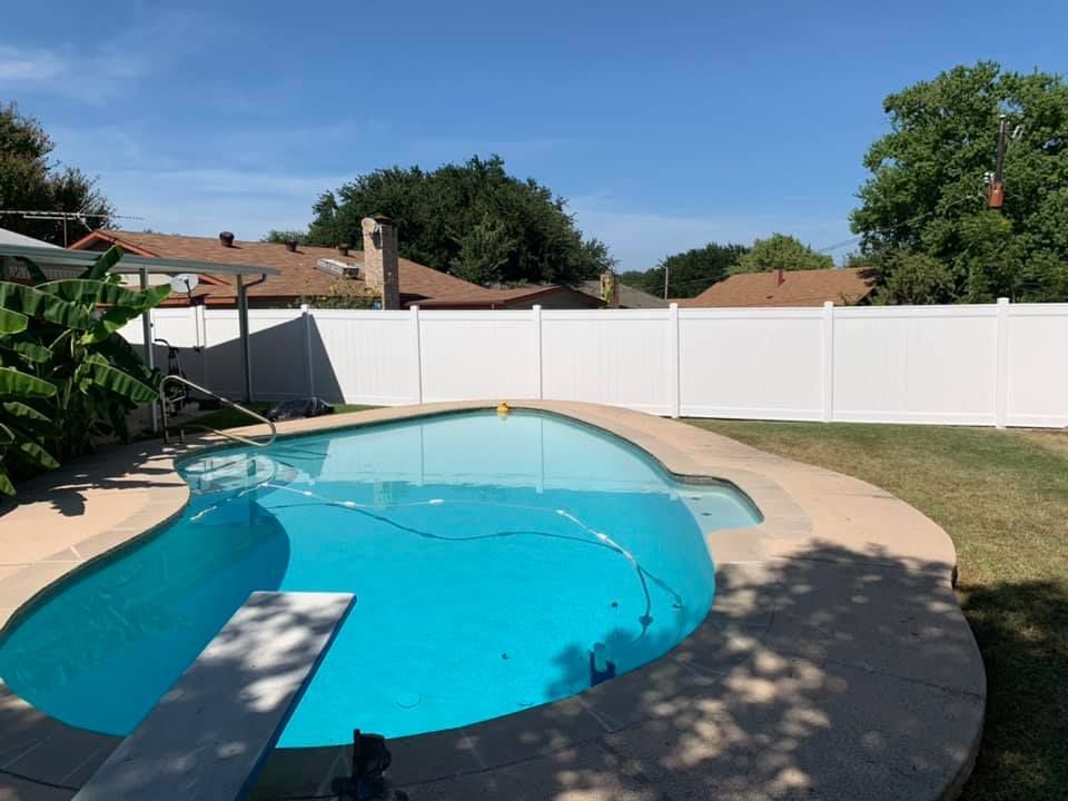 Backyard swimming pool with turquoise water, white fence, and a sunny blue sky