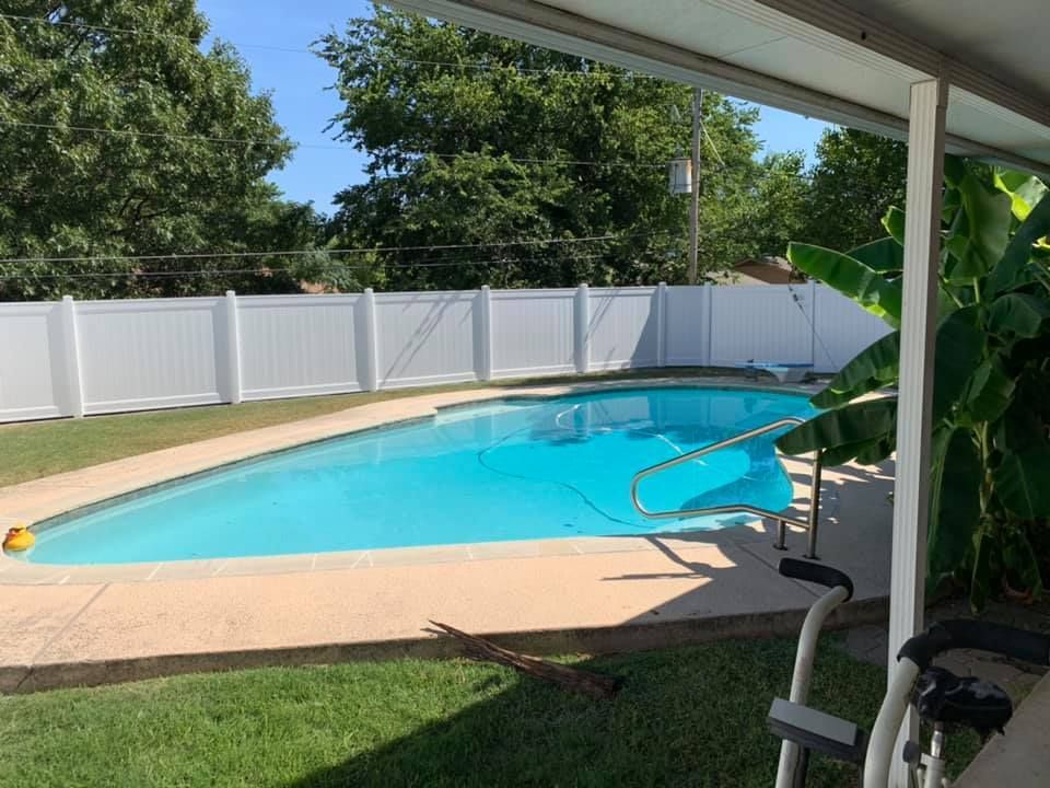 Backyard pool with turquoise water, white fence, and covered patio in the foreground