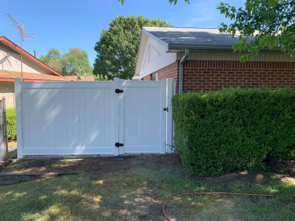 White privacy gate beside a brick house and tall hedge in a sunny residential yard