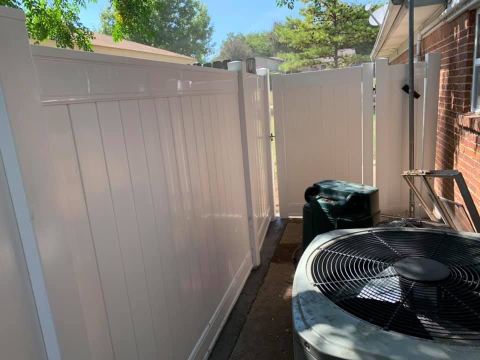 Narrow backyard beside a white fence, with an air conditioner unit and brick house wall.
