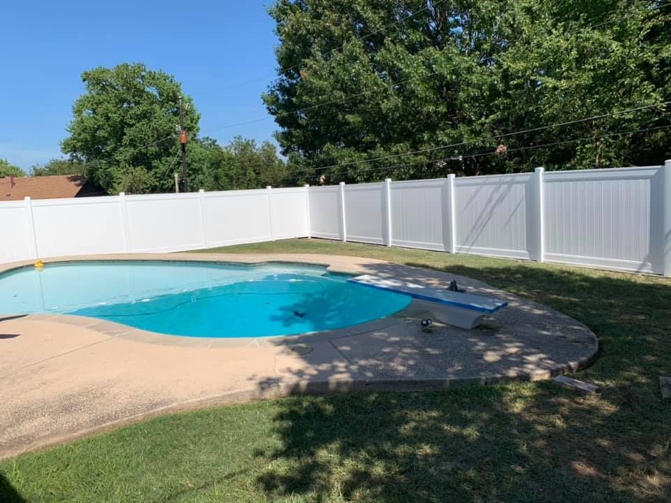 Backyard pool with blue water, white privacy fence, and patio surrounded by grass and trees