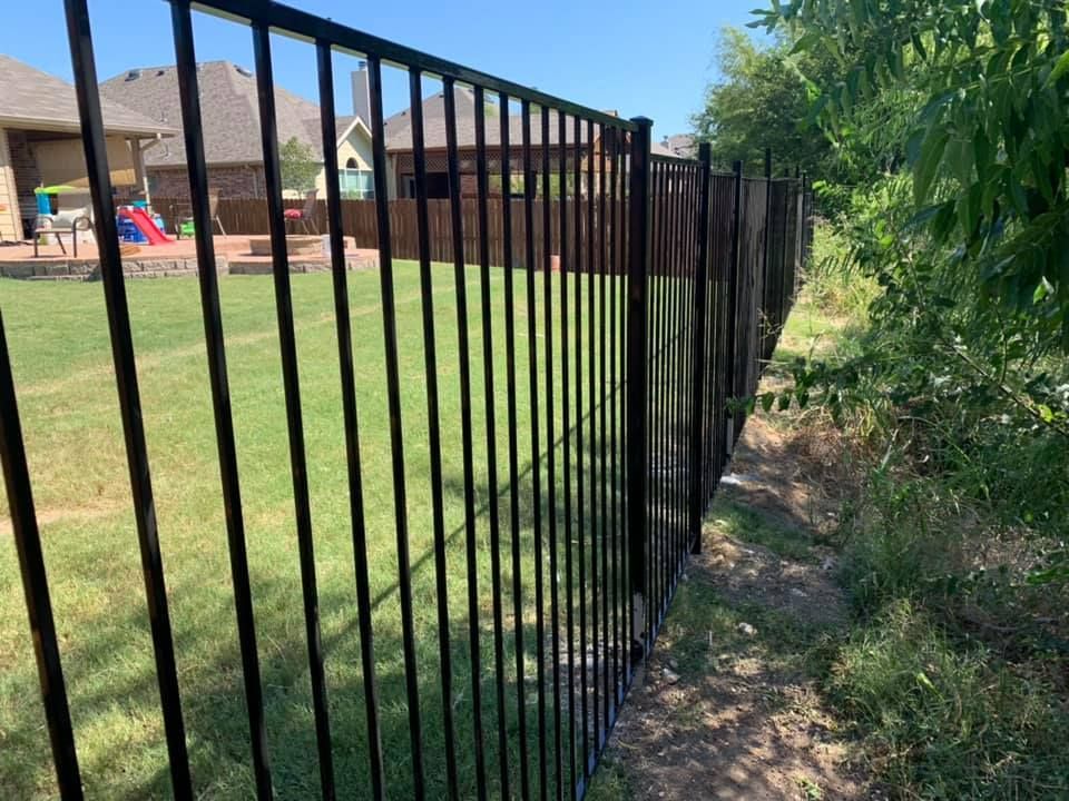 Black metal fence along a grassy backyard beside a house on a sunny day