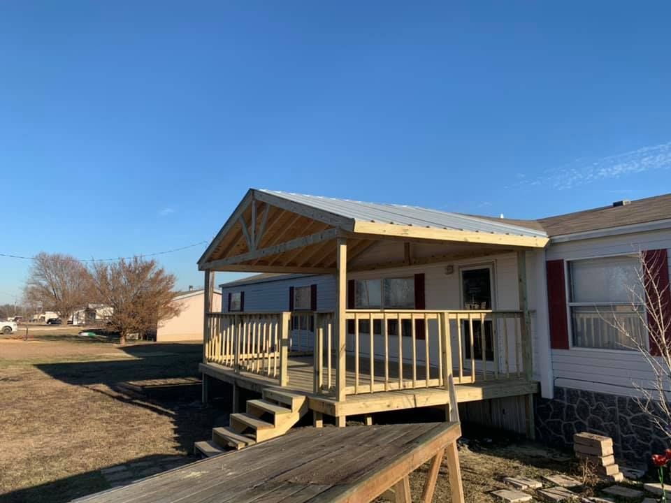 Small porch addition with wooden railing and steps attached to a mobile home under a clear blue sky