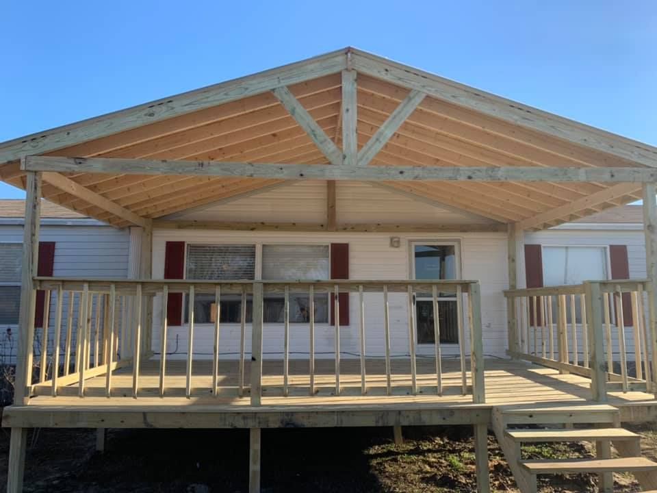 Wooden front porch with railings and steps on a house under construction, framed by a gabled roof.