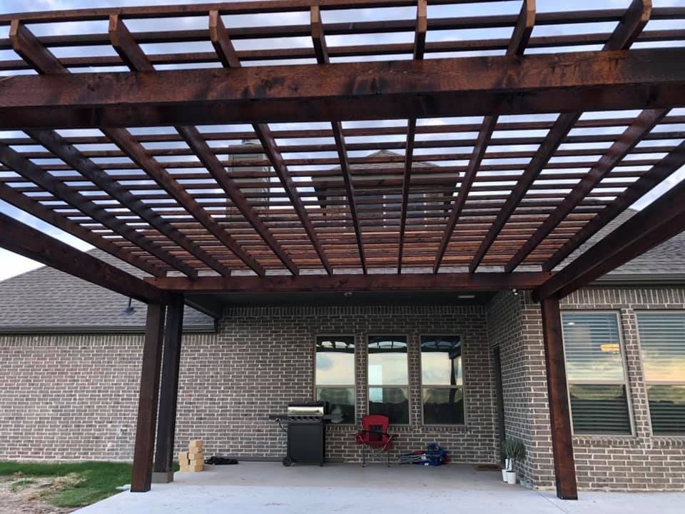 Brick building entrance with a large wooden pergola and glass doors under a covered patio