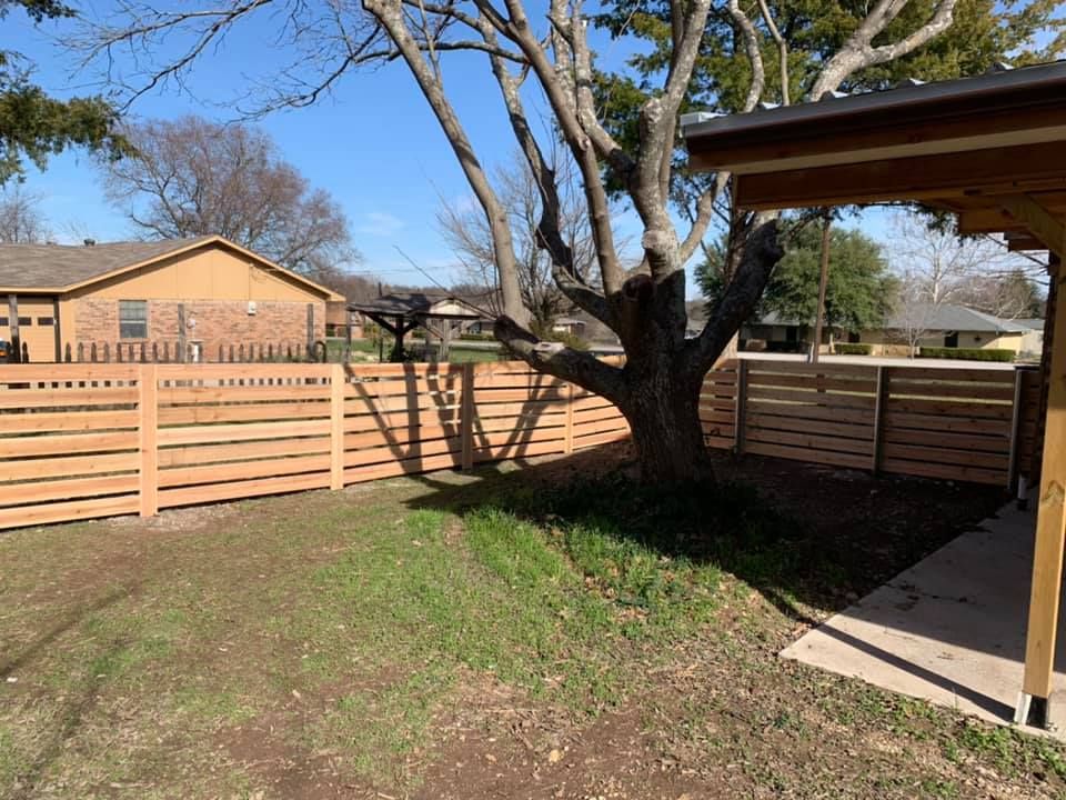 Backyard with wooden privacy fence, large tree, patchy grass, and covered patio
