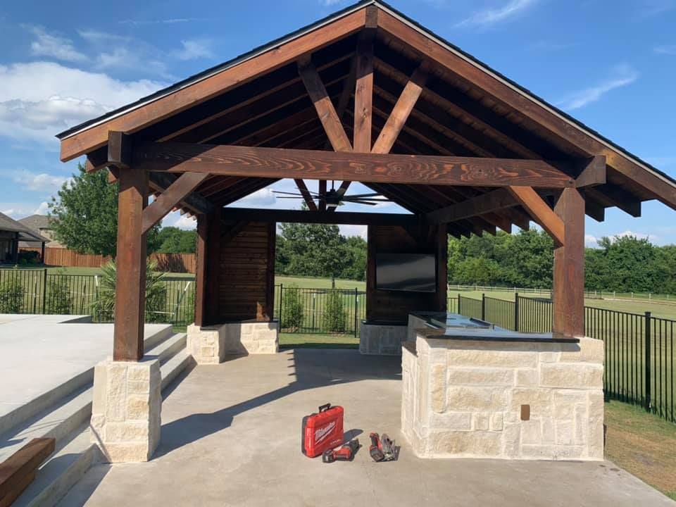 Wooden pavilion with stone walls and red toolbox on a paved outdoor patio.