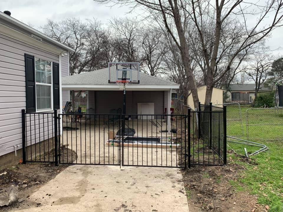 Backyard patio with black metal gate and basketball hoop behind a house