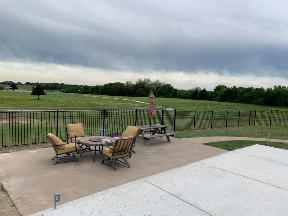 Patio with chairs, tables, and umbrella overlooking a fenced green field under cloudy skies