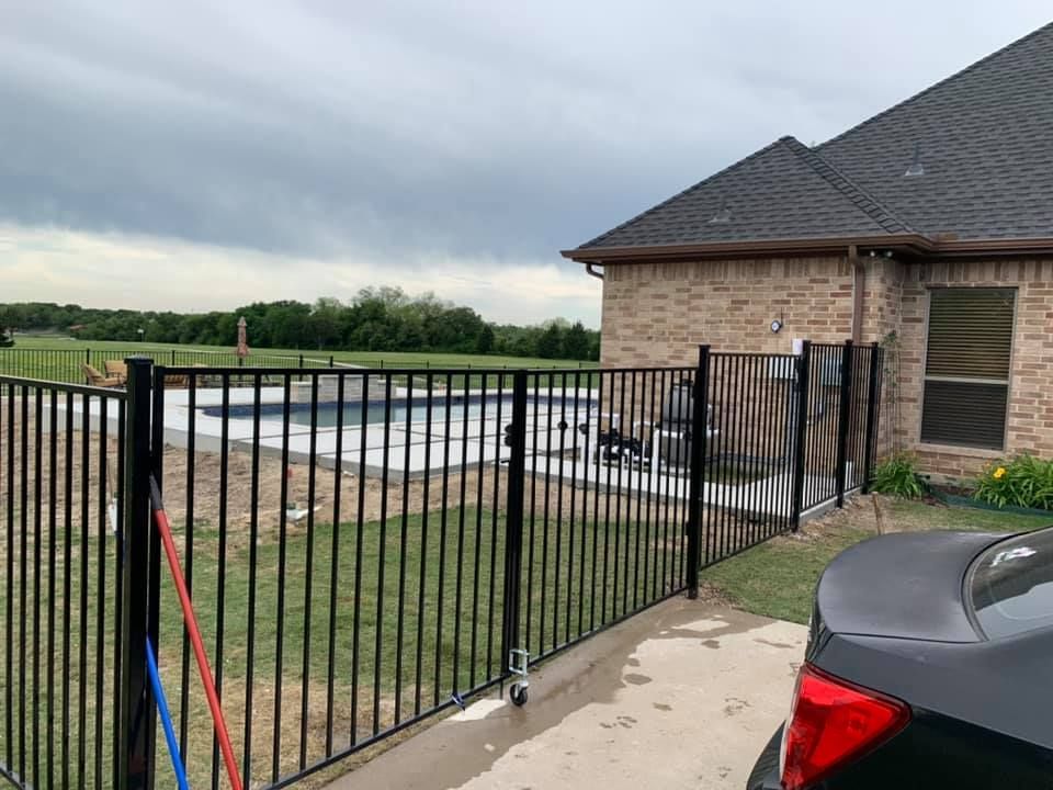 Black metal fence by a brick house beside a backyard pool under cloudy skies.