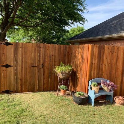 Backyard with wooden fence, green lawn, and potted plants beside a blue chair