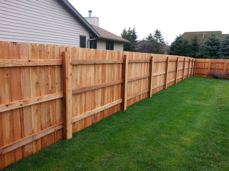 Wooden privacy fence running along a green lawn beside a house and trees