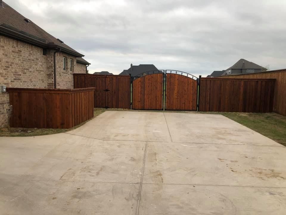 Empty concrete driveway leading to a closed wooden gate between brick houses under a cloudy sky