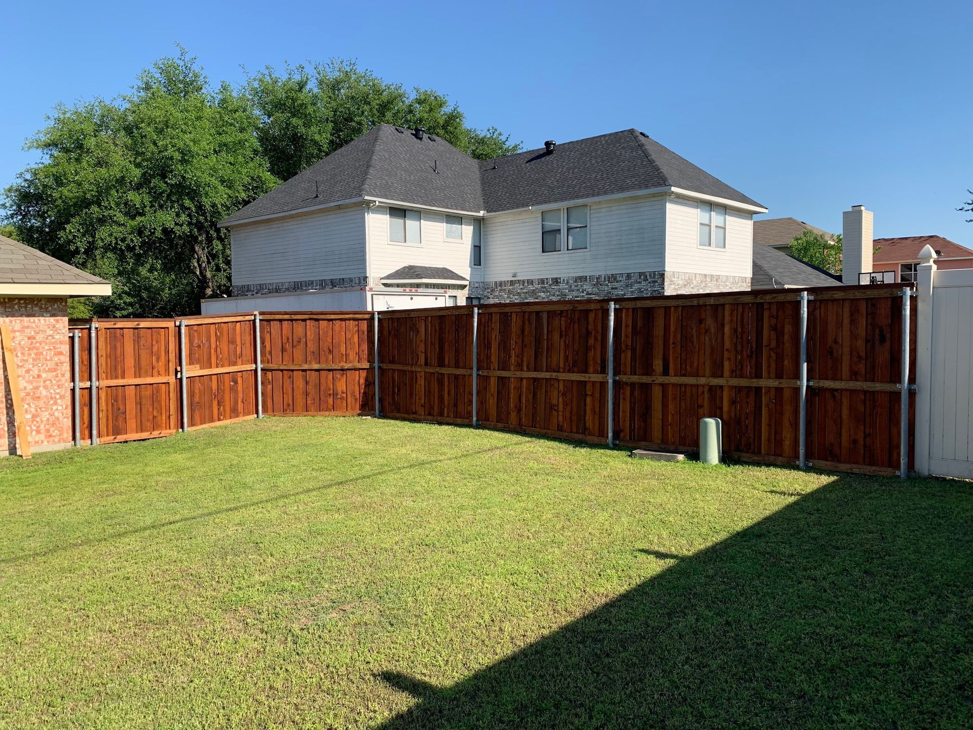Backyard with green lawn, tall wooden fence, and two-story houses in the background