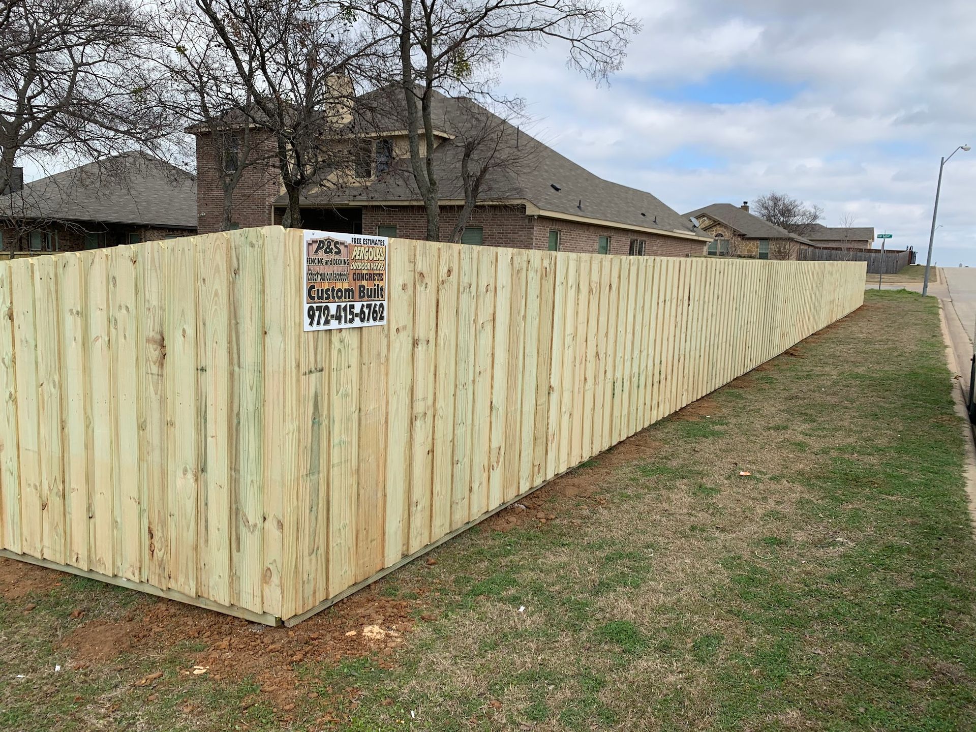 Fresh wooden privacy fence along a sidewalk beside houses on a cloudy day