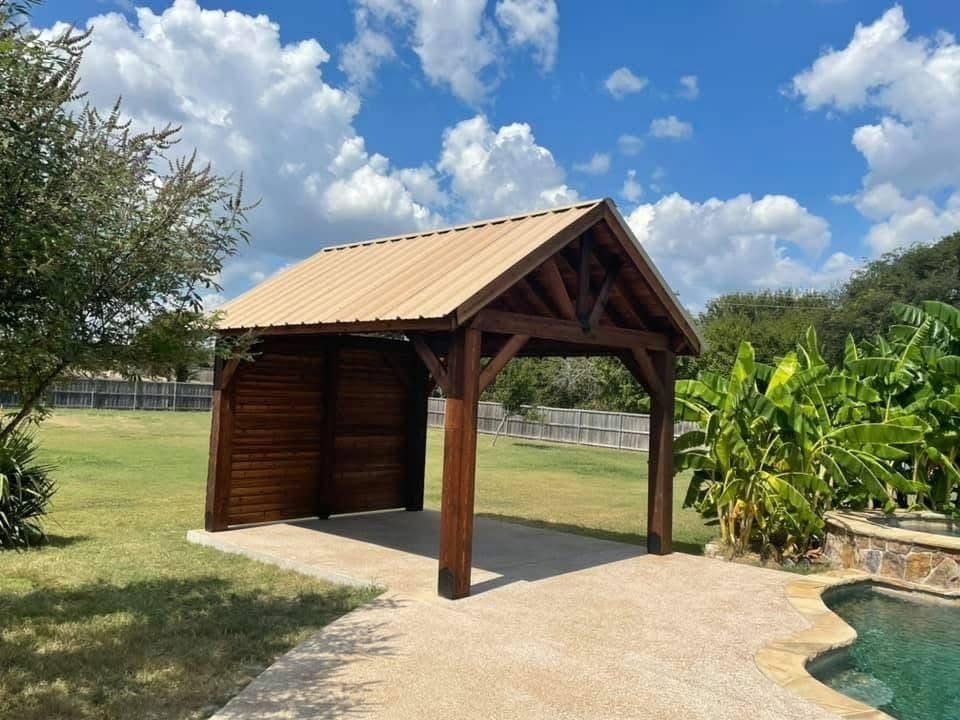 Wooden gazebo beside a pool on a sunny lawn under a blue sky with clouds