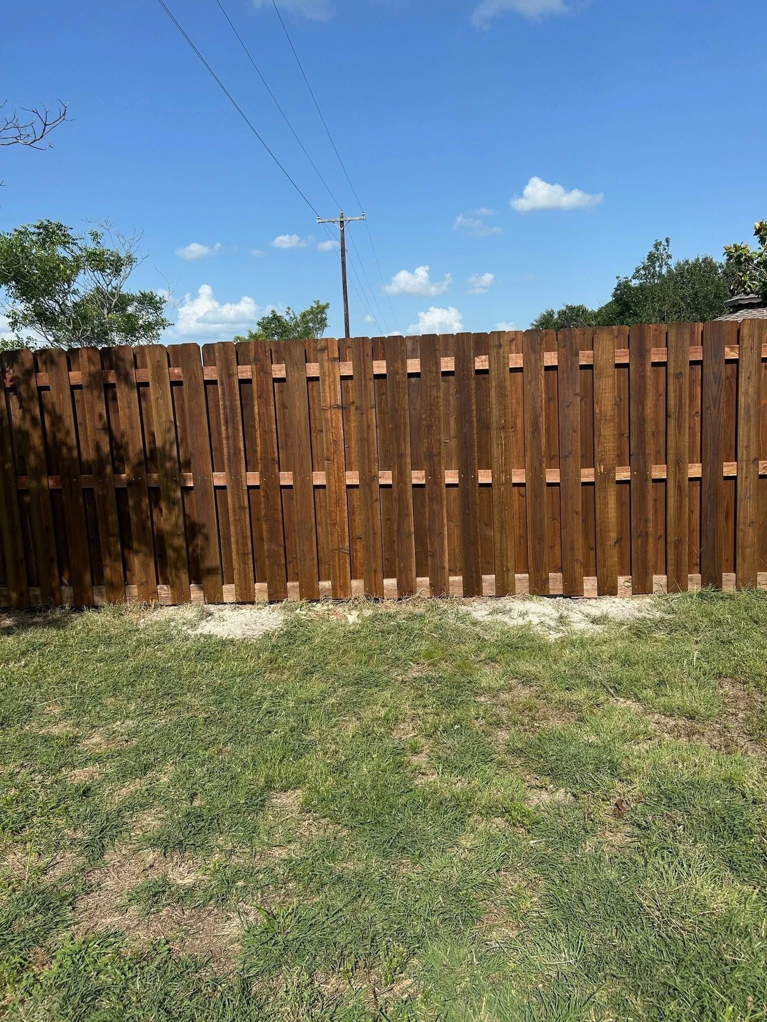 Wooden privacy fence with grassy yard under a blue sky with clouds