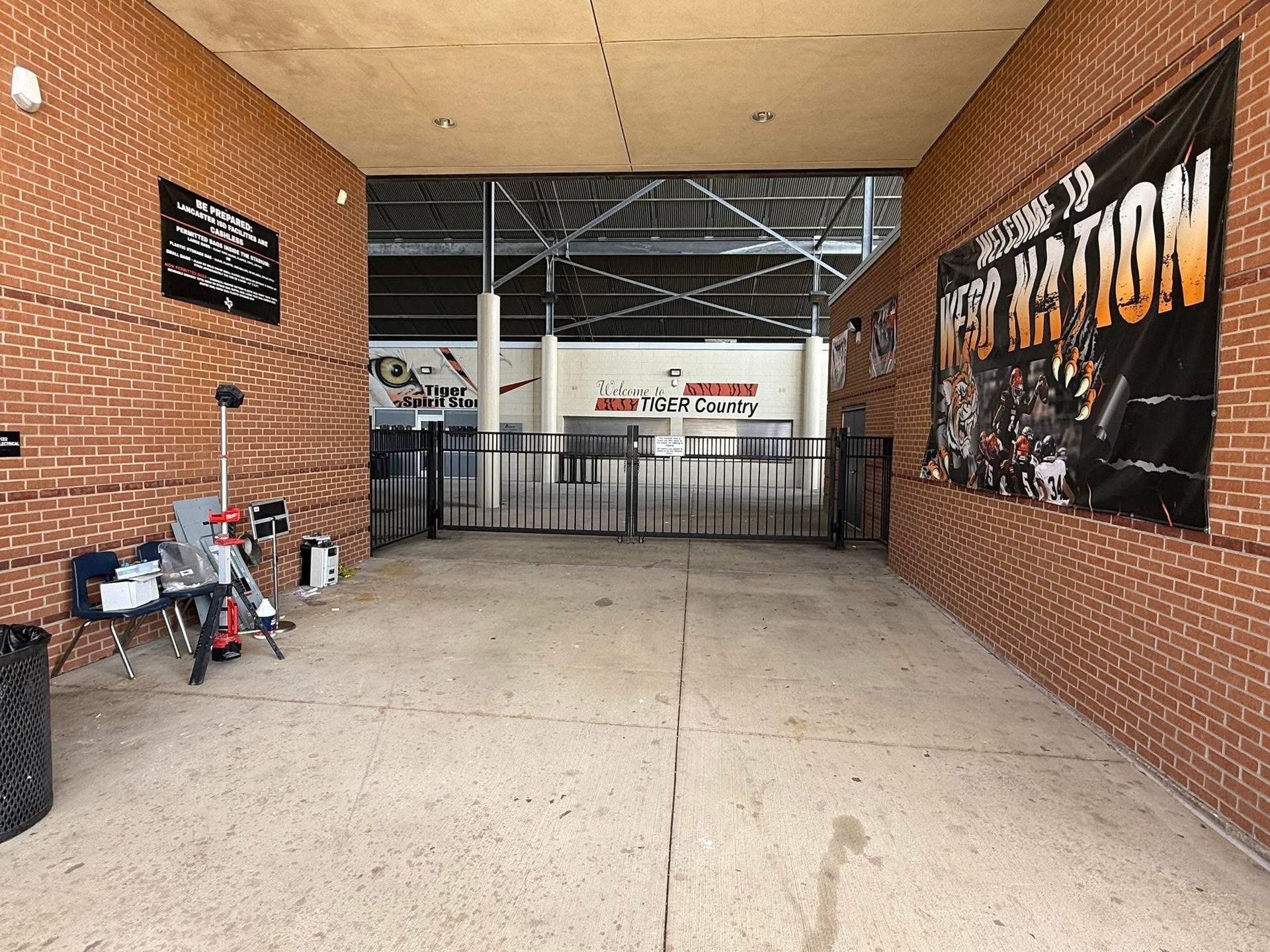 Covered brick hallway with a closed gate, parked motorcycle, and large black event banner on the right