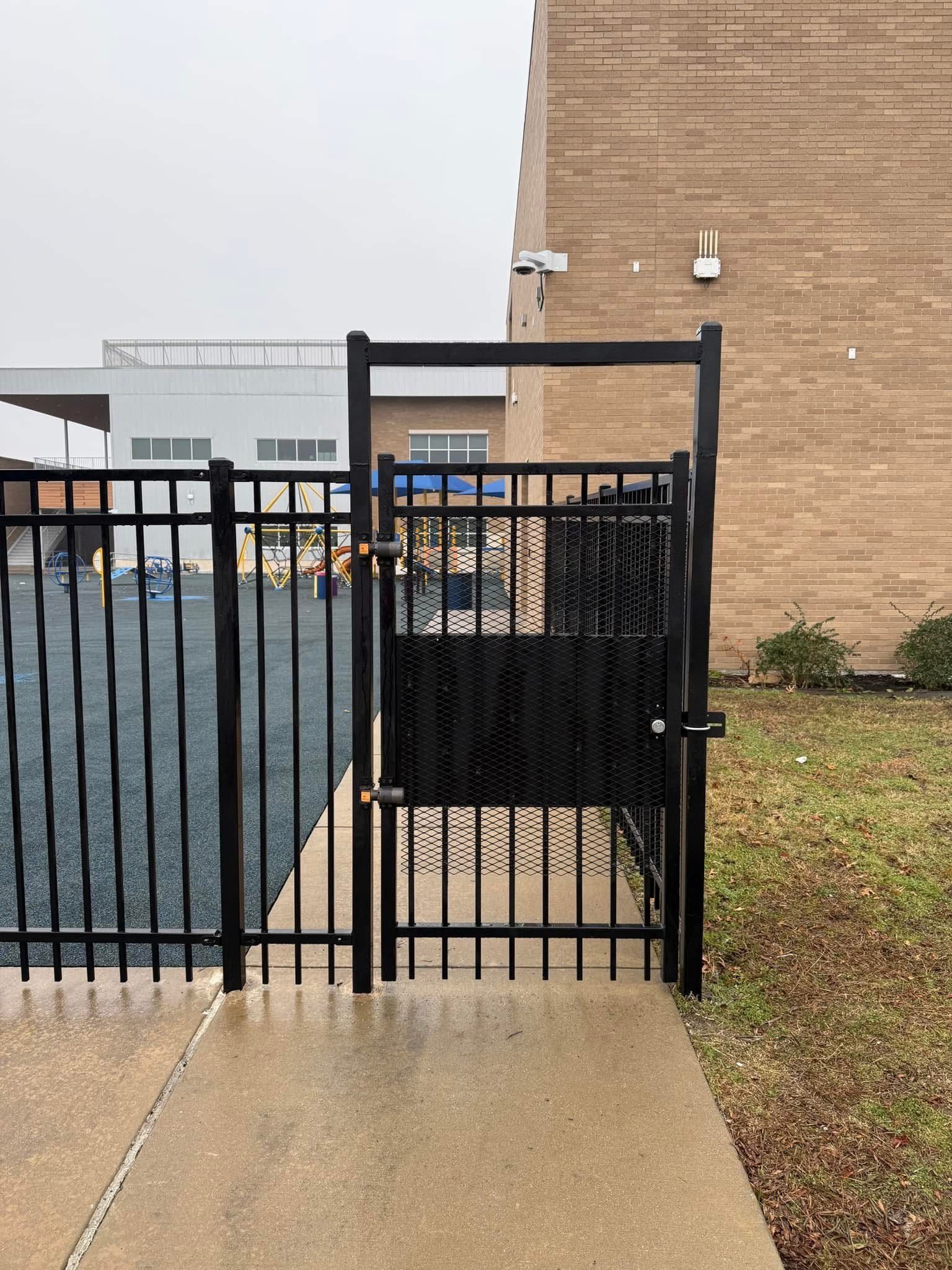 Black metal gate beside a concrete sidewalk and tan brick building