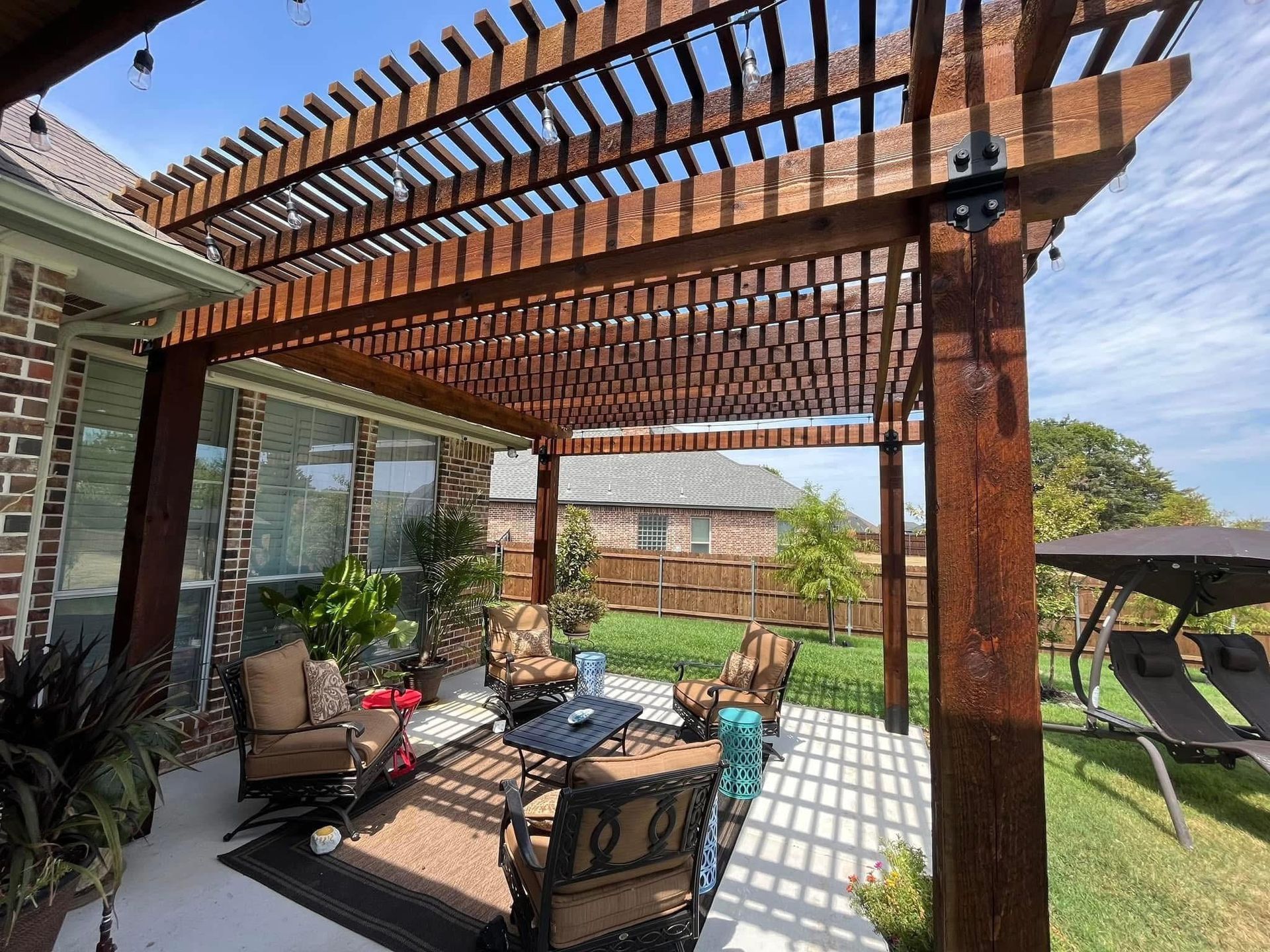 Backyard patio with pergola, outdoor seating, brick grill, and a grassy lawn in sunlight