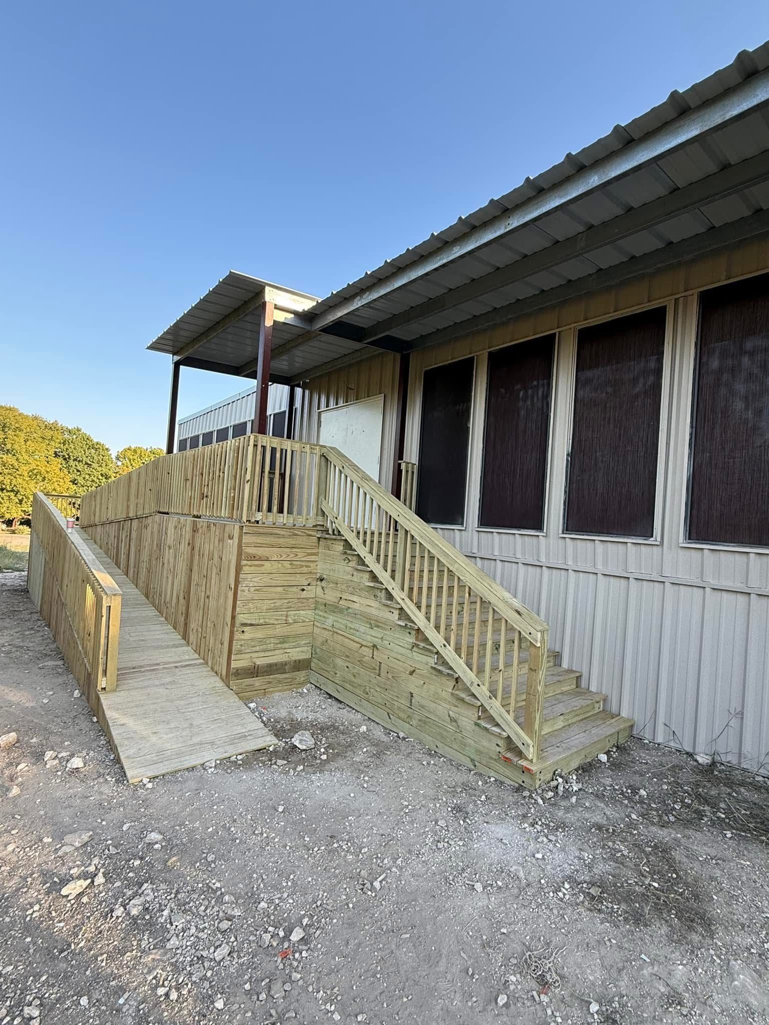 Wooden wheelchair ramp with railings beside a white building on a gravel lot