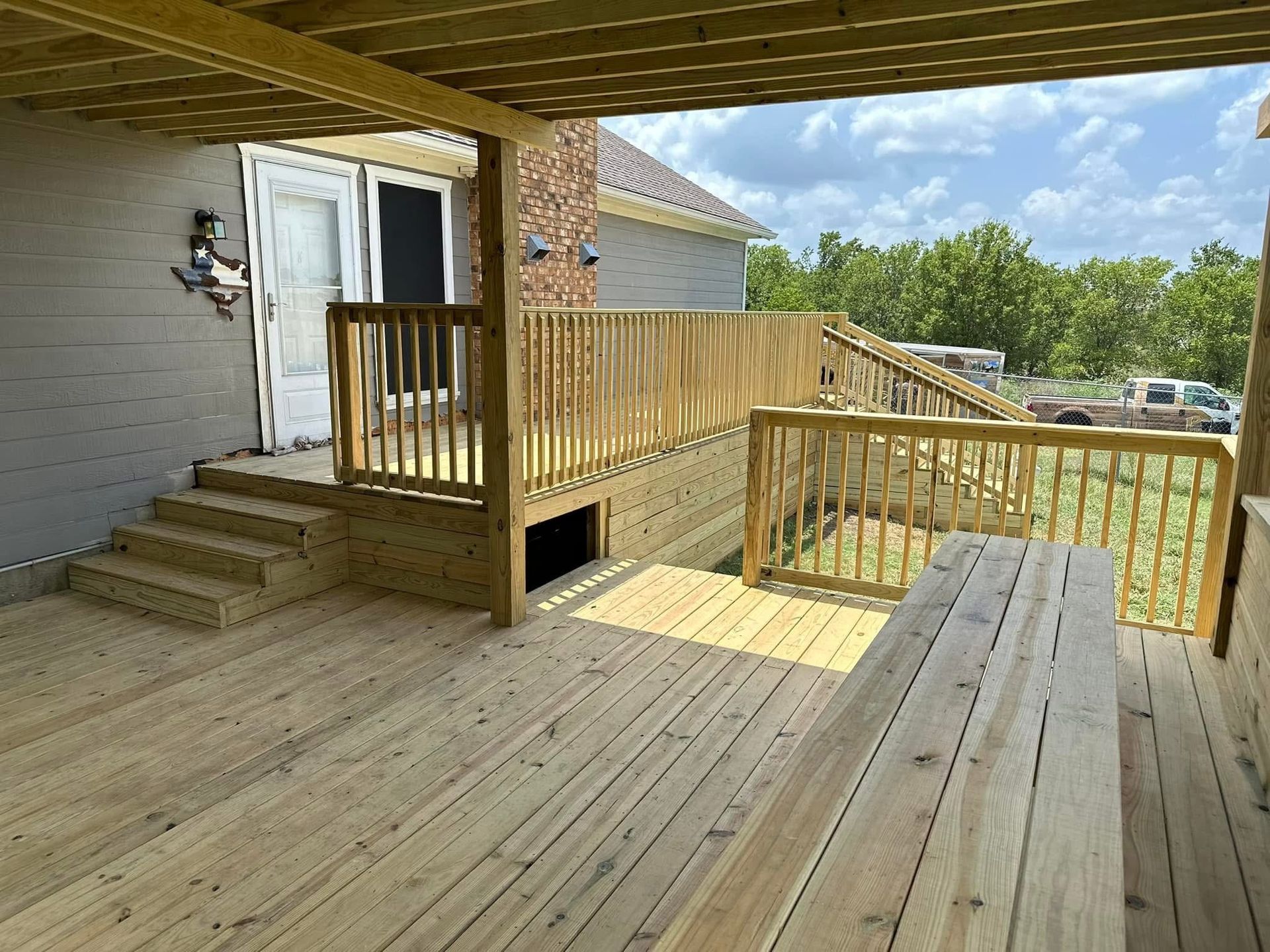 Wooden deck with ramp and railing beside a house, leading to a doorway under a covered porch.