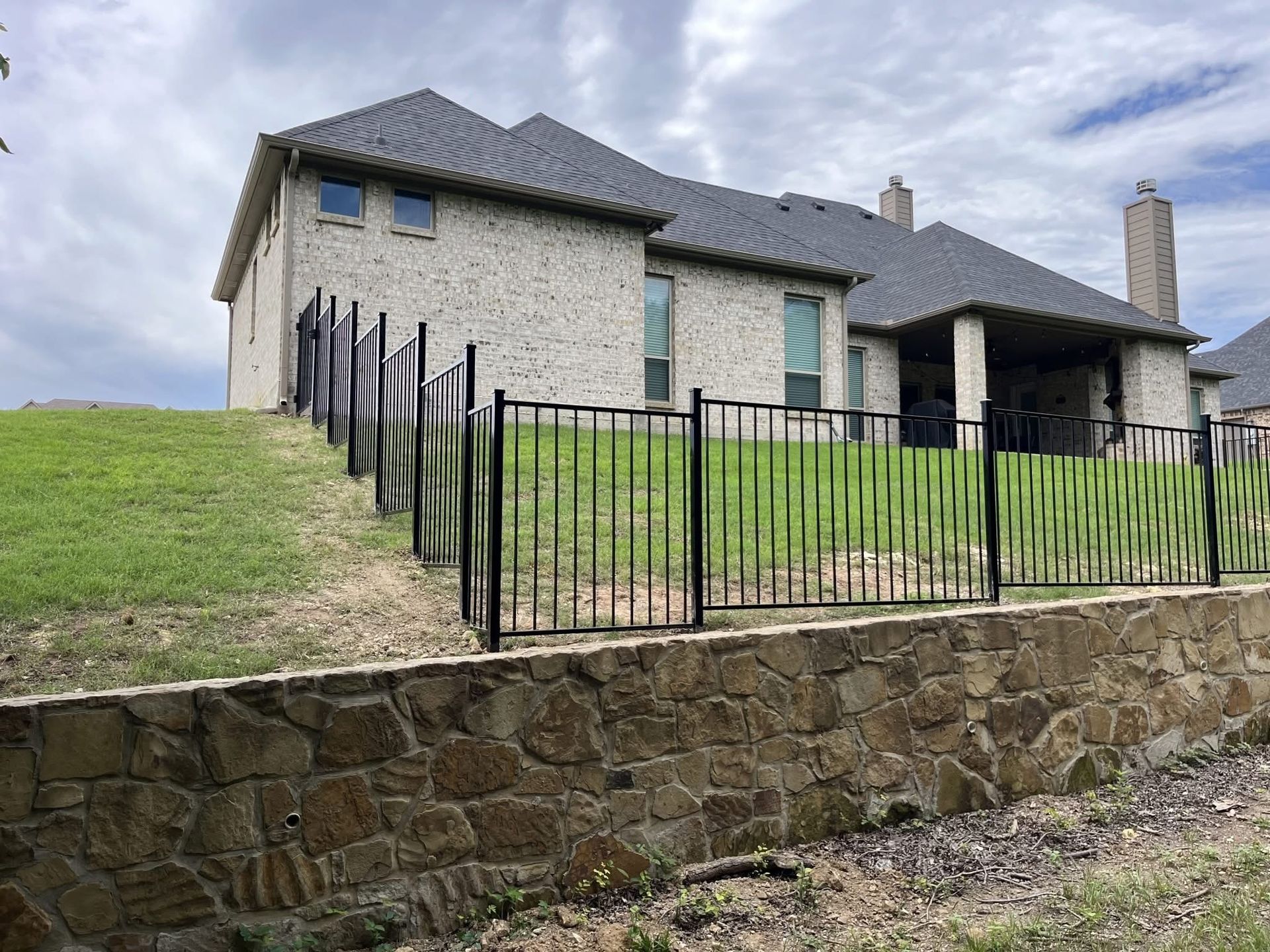Stone house with gray roof behind a black fence on a grassy hillside
