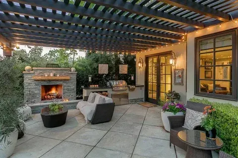 Covered patio with stone fireplace, lounge chairs, and potted plants at dusk