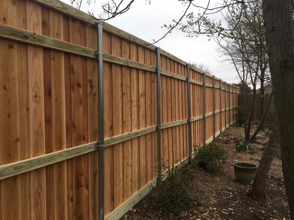 Wooden privacy fence lining a narrow backyard path beside trees and potted plants.