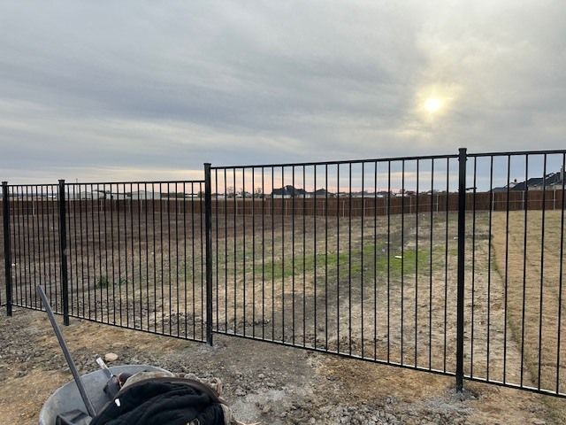 Black metal fence bordering a dry, open field under a cloudy sky