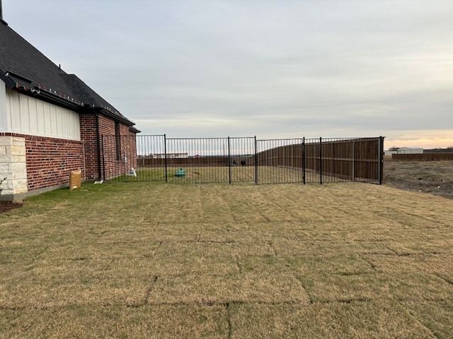 Backyard lawn beside a brick house, fenced along the edge under a cloudy sky.