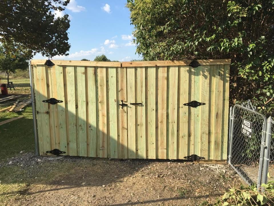 Weathered pale green wooden shed with double doors and black handles in a grassy yard