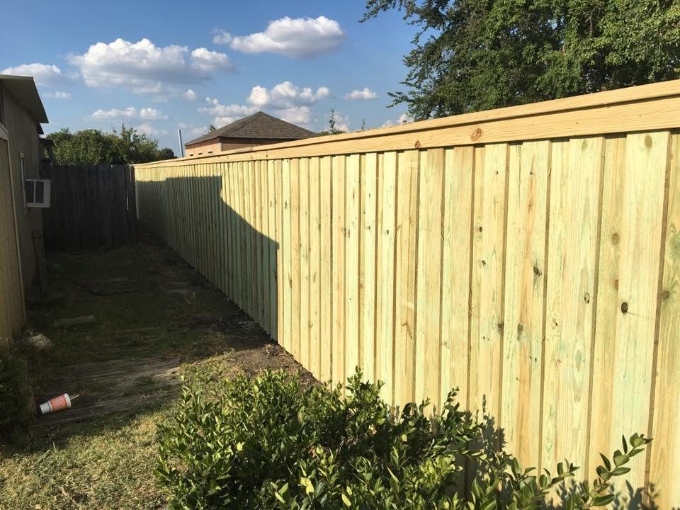 Backyard with a new wooden fence, grass strip, and shrubs under a partly cloudy sky